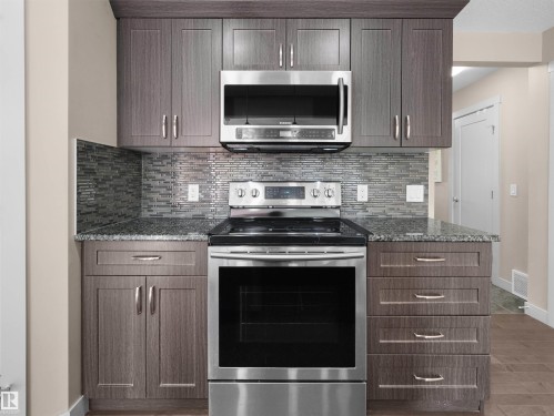 Contemporary kitchen featuring stainless steel appliances, grey wood-finish cabinetry, a mosaic tile backsplash, and stone countertops - 4487 Annett Common Sw, Edmonton, AB - Indoor Photo Showing Kitchen With Upgraded Kitchen