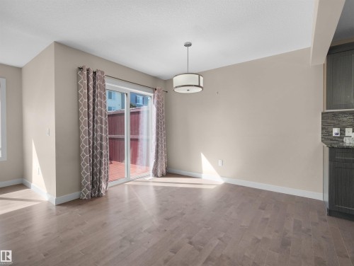 Spacious room featuring wood-finish flooring, a contemporary drum pendant light fixture, and a sliding glass patio door - 4487 Annett Common Sw, Edmonton, AB - Indoor Photo Showing Other Room