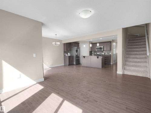 Open-concept living area featuring wood-finish flooring, a kitchen with dark cabinetry and stainless steel appliances, and a carpeted staircase - 4487 Annett Common Sw, Edmonton, AB - Indoor Photo Showing Other Room