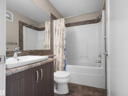 Bathroom featuring a white drop-in sink, wood-finish vanity with dual cabinets, and a decorative tile backsplash - 4487 Annett Common Sw, Edmonton, AB - Indoor Photo Showing Bathroom