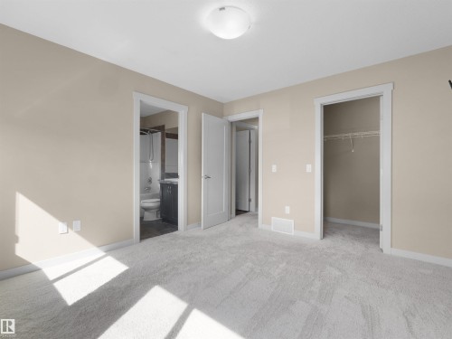Carpeted room featuring a ceiling-mounted light fixture, neutral wall paint, white trim, and a white interior door - 4487 Annett Common Sw, Edmonton, AB - Indoor Photo Showing Other Room