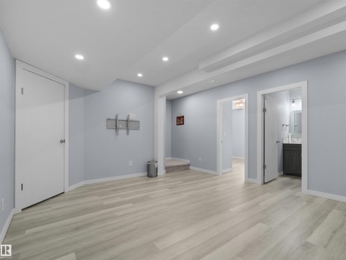 Spacious room featuring light wood-finish flooring, recessed lighting, light blue wall paint, white trim, and a white paneled door - 4487 Annett Common Sw, Edmonton, AB - Indoor Photo Showing Other Room