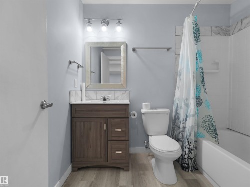 Bathroom featuring a wood-finish vanity with a white countertop and integrated sink, framed mirror, and chrome fixtures - 4487 Annett Common Sw, Edmonton, AB - Indoor Photo Showing Bathroom
