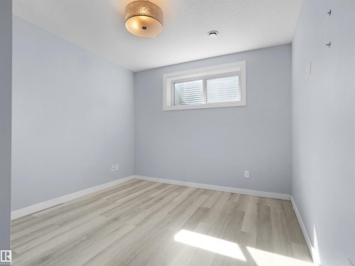 Spacious room featuring light wood-finish flooring, light blue painted walls, a flush-mount ceiling light fixture, and a window with horizontal blinds - 4487 Annett Common Sw, Edmonton, AB - Indoor Photo Showing Other Room