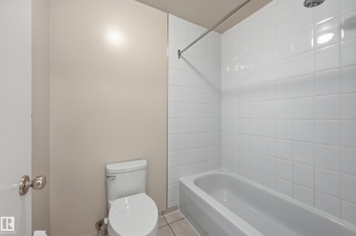 Bathroom featuring a full-size bathtub, white subway tile surround, white toilet, and tile flooring - #433 11217 103 Av Nw, Edmonton, AB - Indoor Photo Showing Bathroom