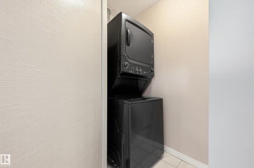 Dedicated laundry area featuring a stacked black washer and dryer unit, neutral wall paint, and tiled flooring - #433 11217 103 Av Nw, Edmonton, AB - Indoor Photo Showing Laundry Room
