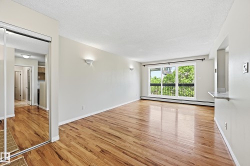 Spacious living area featuring expansive wood-finish flooring, a large window with a black wrought iron balcony, and two wall sconces - #433 11217 103 Av Nw, Edmonton, AB - Indoor Photo Showing Other Room