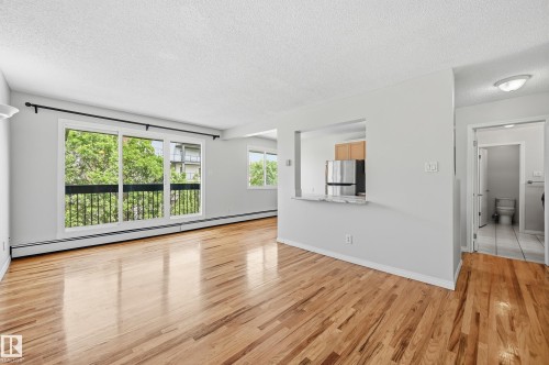 Spacious living area featuring wood-finish flooring, white baseboards, and a neutral color palette - #433 11217 103 Av Nw, Edmonton, AB - Indoor Photo Showing Other Room