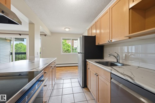 Kitchen featuring light wood cabinetry, stone-finish countertops, stainless steel appliances, and tile flooring - #433 11217 103 Av Nw, Edmonton, AB - Indoor Photo Showing Kitchen