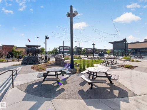 Outdoor common area featuring multiple picnic tables, paved walkways, and a central lawn space - #217 12045 22 Av Sw, Edmonton, AB - Outdoor With View