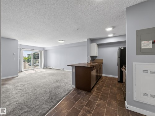 Open-concept living space featuring a sliding glass door to a private balcony, light gray carpeting, and recessed lighting - #217 12045 22 Av Sw, Edmonton, AB - Indoor