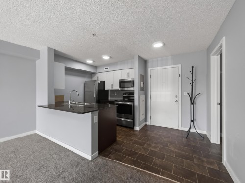 Kitchen featuring stainless steel appliances, dark countertop, and light cabinetry - #217 12045 22 Av Sw, Edmonton, AB - Indoor Photo Showing Kitchen With Stainless Steel Kitchen