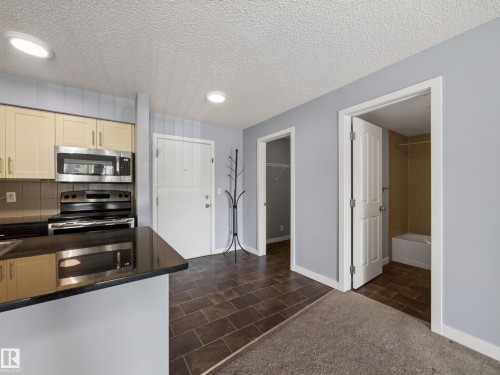 Contemporary kitchen featuring stainless steel appliances, light-toned cabinetry, and dark countertops - #217 12045 22 Av Sw, Edmonton, AB - Indoor Photo Showing Kitchen