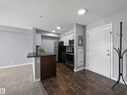 Kitchenette featuring white cabinetry, black appliances, a stainless steel sink, and a black countertop on a breakfast bar - 