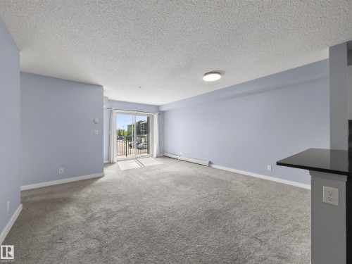 Spacious room featuring light blue walls, grey carpeting, and a sliding glass door leading to a balcony - #217 12045 22 Av Sw, Edmonton, AB - Indoor Photo Showing Other Room