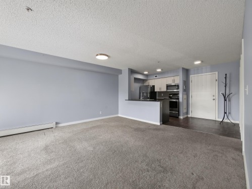 Open-concept living space with light gray carpeting and blue-gray walls - #217 12045 22 Av Sw, Edmonton, AB - Indoor