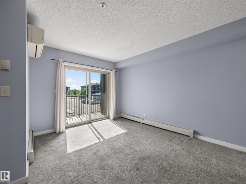 Sliding glass doors opening to an outdoor balcony with black metal railings - #217 12045 22 Av Sw, Edmonton, AB - Indoor Photo Showing Other Room