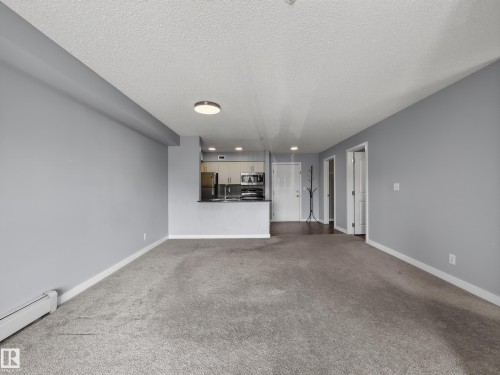 Open-concept living space featuring light gray walls, textured carpet flooring, and white trim - #217 12045 22 Av Sw, Edmonton, AB - Indoor Photo Showing Other Room