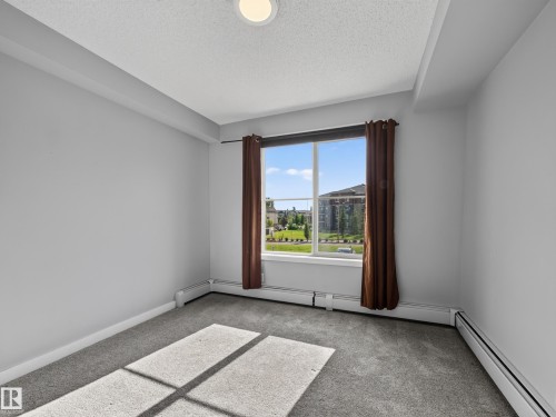 Bright room featuring a large window, plush gray carpeting, baseboard heating, and light gray wall paint - #217 12045 22 Av Sw, Edmonton, AB - Indoor Photo Showing Other Room