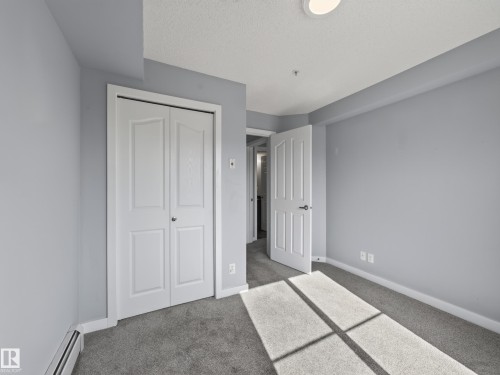 Carpeted room featuring light gray walls, white trim, and a bi-fold closet door - #217 12045 22 Av Sw, Edmonton, AB - Indoor