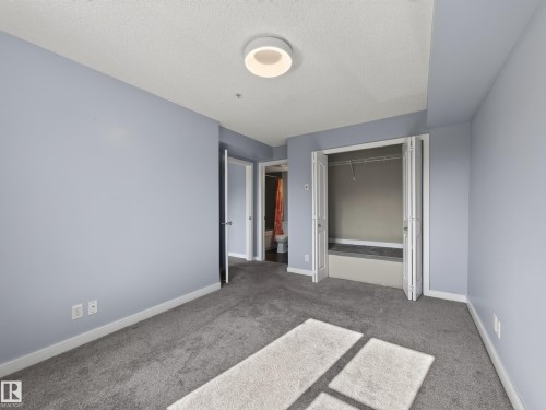 Carpeted room featuring light blue walls, a ceiling-mounted light fixture, white trim, and a bi-fold closet with shelving - #217 12045 22 Av Sw, Edmonton, AB - Indoor Photo Showing Other Room