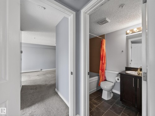 Bathroom featuring dark floor tiles, a white bathtub, a toilet, and a vanity with a dark wood-finish cabinet and a white sink - #217 12045 22 Av Sw, Edmonton, AB - Indoor Photo Showing Bathroom