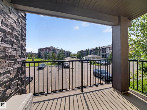 Private balcony featuring a black metal railing, concrete flooring, and a stacked stone wall accent - #217 12045 22 Av Sw, Edmonton, AB - Outdoor With Balcony With Exterior
