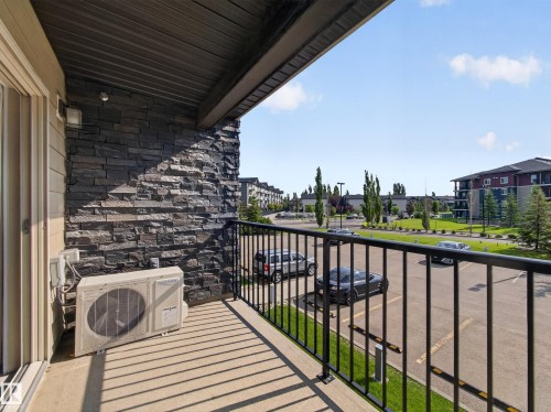 Outdoor balcony featuring a black metal railing and a stone accent wall - #217 12045 22 Av Sw, Edmonton, AB - Outdoor With Balcony With Exterior