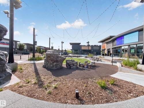 Modern mixed-use development featuring contemporary architecture, stone and wood-paneled facades, and a central green space - #217 12045 22 Av Sw, Edmonton, AB - Outdoor