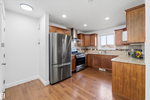Kitchen featuring wood-finish flooring, stainless steel appliances, wood cabinetry, stone countertops, and a tiled backsplash - 2803 12 Street Nw, Edmonton, AB - Indoor Photo Showing Kitchen With Stainless Steel Kitchen