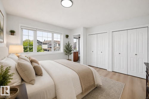 Bedroom featuring light wood-finish flooring, a large multi-pane window, and two sets of white bi-fold closet doors - 2803 12 Street Nw, Edmonton, AB - Indoor Photo Showing Bedroom