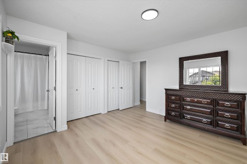 Bright room featuring light wood-finish flooring, multiple white bi-fold closet doors, a ceiling-mounted light fixture, and a partial bathroom with tiled flooring - 2803 12 Street Nw, Edmonton, AB - Indoor