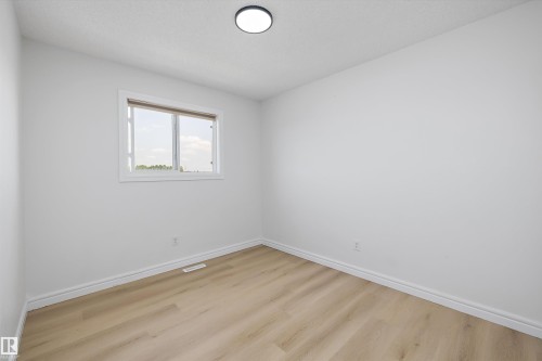 Bright interior space featuring a window with white trim, wood-finish flooring, white baseboards, and a flush-mount ceiling light fixture - 2803 12 Street Nw, Edmonton, AB - Indoor Photo Showing Other Room