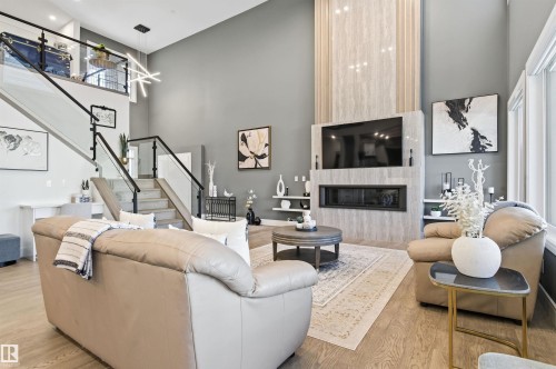 Living room featuring stairs, a fireplace, light wood-style flooring, and a towering ceiling - 3167 Cameron Heights Way Nw, Edmonton, AB - Indoor Photo Showing Living Room With Fireplace