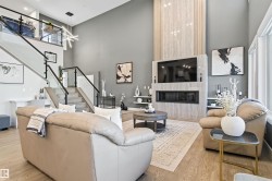 Living room featuring stairs, a fireplace, light wood-style flooring, and a towering ceiling - 
