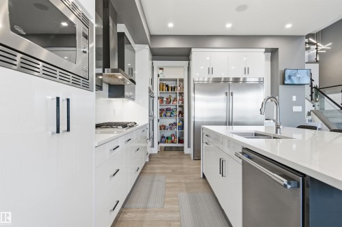 Kitchen with built in appliances, light stone counters, white cabinets, wall chimney range hood, and light wood-style floors - 3167 Cameron Heights Way Nw, Edmonton, AB - Indoor Photo Showing Kitchen With Double Sink With Upgraded Kitchen