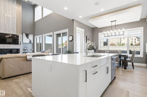 Kitchen with hanging light fixtures, light stone counters, white cabinets, a kitchen island with sink, and modern cabinets - 3167 Cameron Heights Way Nw, Edmonton, AB - Indoor Photo Showing Other Room