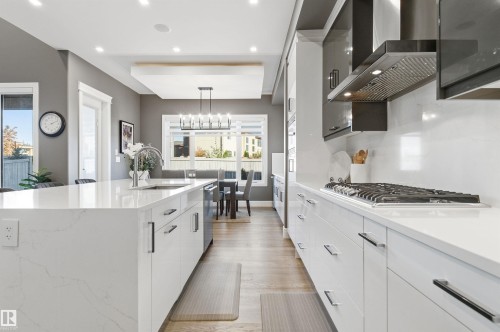 Kitchen with wall chimney range hood, white cabinets, light stone counters, pendant lighting, and recessed lighting - 3167 Cameron Heights Way Nw, Edmonton, AB - Indoor Photo Showing Kitchen With Upgraded Kitchen