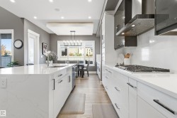 Kitchen with wall chimney range hood, white cabinets, light stone counters, pendant lighting, and recessed lighting - 