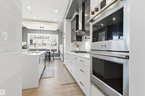 Kitchen featuring appliances with stainless steel finishes, modern cabinets, pendant lighting, light stone counters, and light wood-type flooring - 3167 Cameron Heights Way Nw, Edmonton, AB - Indoor Photo Showing Kitchen