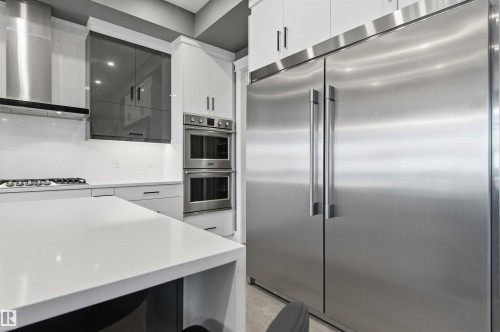 Kitchen featuring stainless steel appliances, wall chimney range hood, white cabinets, light stone counters, and modern cabinets - 3167 Cameron Heights Way Nw, Edmonton, AB - Indoor Photo Showing Kitchen With Upgraded Kitchen