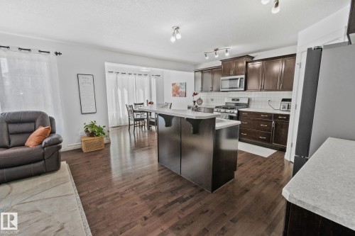 Open concept living area featuring dark wood flooring, a kitchen with dark cabinetry, stainless steel appliances, and an island with a light-colored countertop - 1115 61 Street Sw, Edmonton, AB - Indoor Photo Showing Kitchen With Upgraded Kitchen