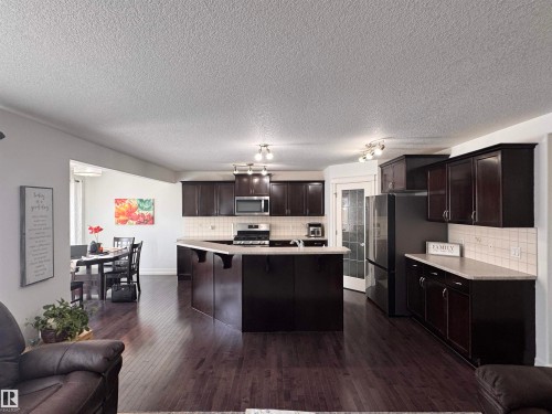 Kitchen featuring dark wood cabinetry, stainless steel appliances, a center island with seating, and light countertops - 1115 61 Street Sw, Edmonton, AB - Indoor Photo Showing Other Room