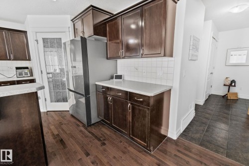 The kitchen features wood cabinetry, a stainless steel refrigerator, white tile backsplash, and light-colored countertops - 1115 61 Street Sw, Edmonton, AB - Indoor Photo Showing Kitchen