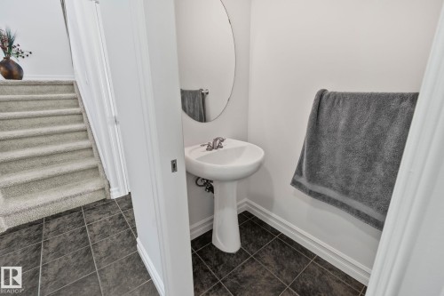 The property features a powder room with a pedestal sink and an oval mirror, complemented by dark tile flooring - 1115 61 Street Sw, Edmonton, AB - Indoor Photo Showing Bathroom