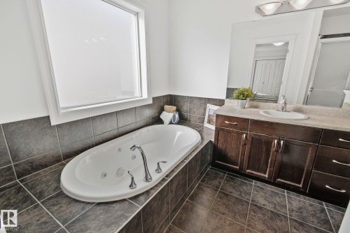 Bathroom featuring a built-in jetted tub, a window with privacy glass, a vanity with a single sink and a mirror, and tiled floors - 1115 61 Street Sw, Edmonton, AB - Indoor Photo Showing Bathroom