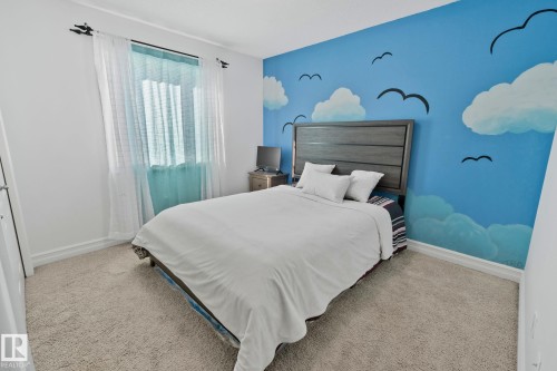 Bedroom featuring light-colored carpet flooring, white walls, and a feature wall with a blue sky and cloud mural - 1115 61 Street Sw, Edmonton, AB - Indoor Photo Showing Bedroom