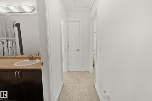 Hallway with neutral carpeting and white walls leading to a bathroom featuring a vanity with a light-colored countertop and a mirror - 1115 61 Street Sw, Edmonton, AB - Indoor Photo Showing Bathroom