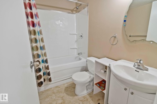This bathroom features a white bathtub with a shower, a toilet, and a vanity with a sink and mirror - 1115 61 Street Sw, Edmonton, AB - Indoor Photo Showing Bathroom