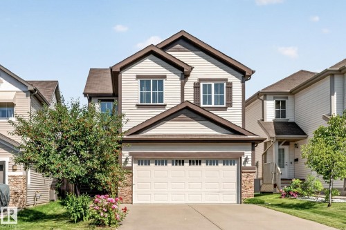 Two-story residence featuring light-colored siding with contrasting trim, a prominent front-facing garage, and decorative stone accents - 1115 61 Street Sw, Edmonton, AB - Outdoor With Facade